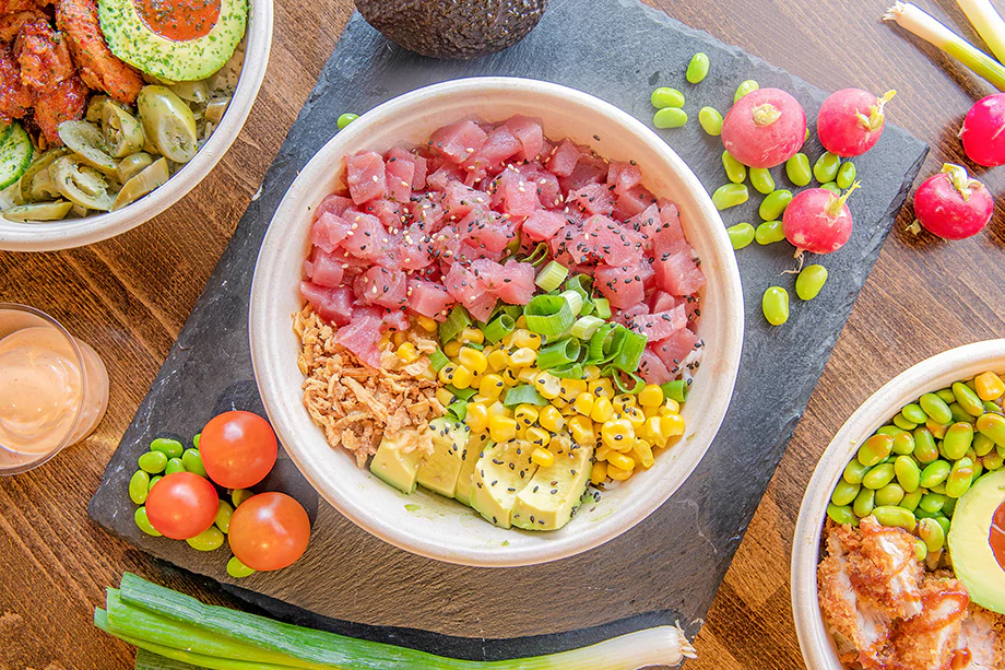A bright looking poke bowl surrounded by other various types of Japanese food.