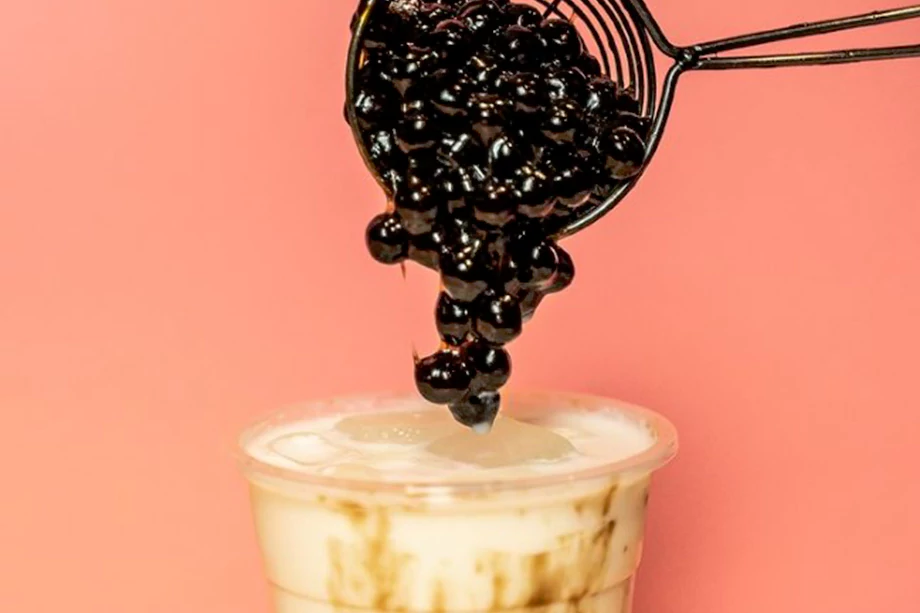An image of bubble tea with tropical pearls poured on top in front of an orange background.