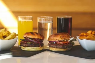 An image of Piri Piri Beef Burgers and some drinks with a side of chips