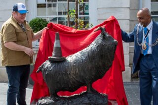 revealing a bronze goat sculpture underneath a red cloth