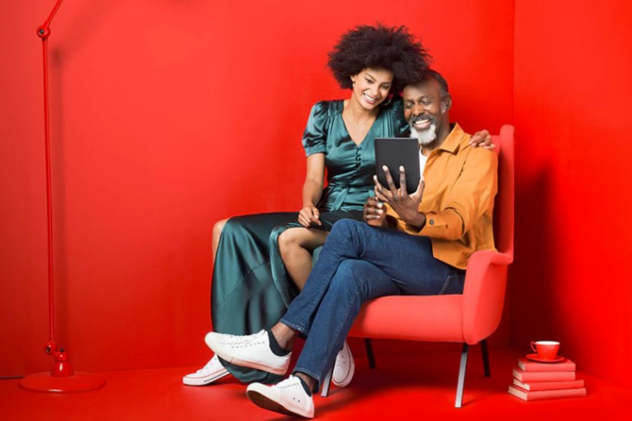 An image of an elder man and a younger woman using a tablet on a sofa